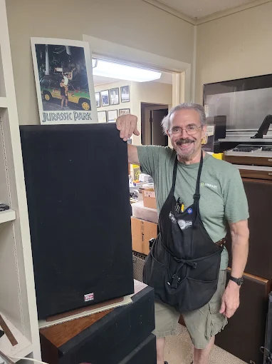 A Speakerworks repair technician in a work apron standing beside a large speaker.